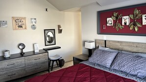 Ett sovrum med en säng, ett skrivbord och en stol. Det finns dekorationer på väggarna, bland annat inramade bilder och en spegel.