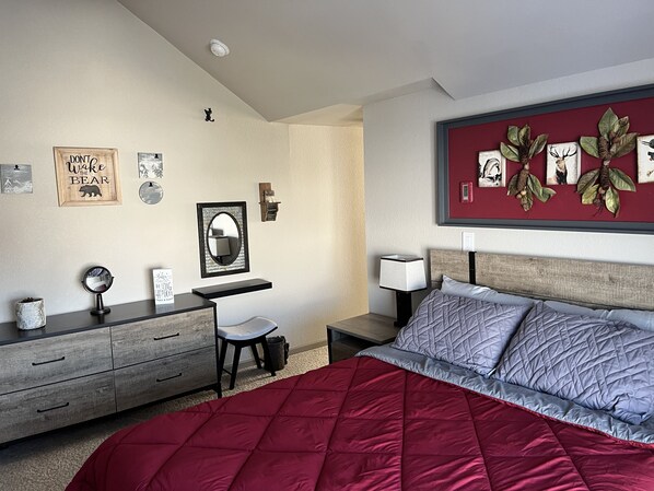 Een slaapkamer met een bed, een bureau, een stoel, een dressoir en wanddecoraties, waaronder ingelijste foto's en een spiegel.