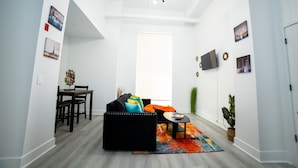 A modern living room with a black sofa, colorful cushions, a dining table with chairs, and a vibrant rug. - 💎 Sanitized*LUXURY* Relaxing*MODERN APT In the HEART OF DOWNTOWN (Baltimore)
