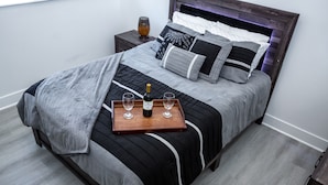 A neatly made bed with a tray holding a bottle and glasses, a bedside table with a lamp, and a headboard with decorative pillows. - 💎 Sanitized*LUXURY* Relaxing*MODERN APT In the HEART OF DOWNTOWN (Baltimore)