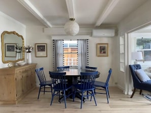 Uma sala de jantar com uma mesa redonda e cadeiras azuis, um armário de madeira e um espelho grande na parede.