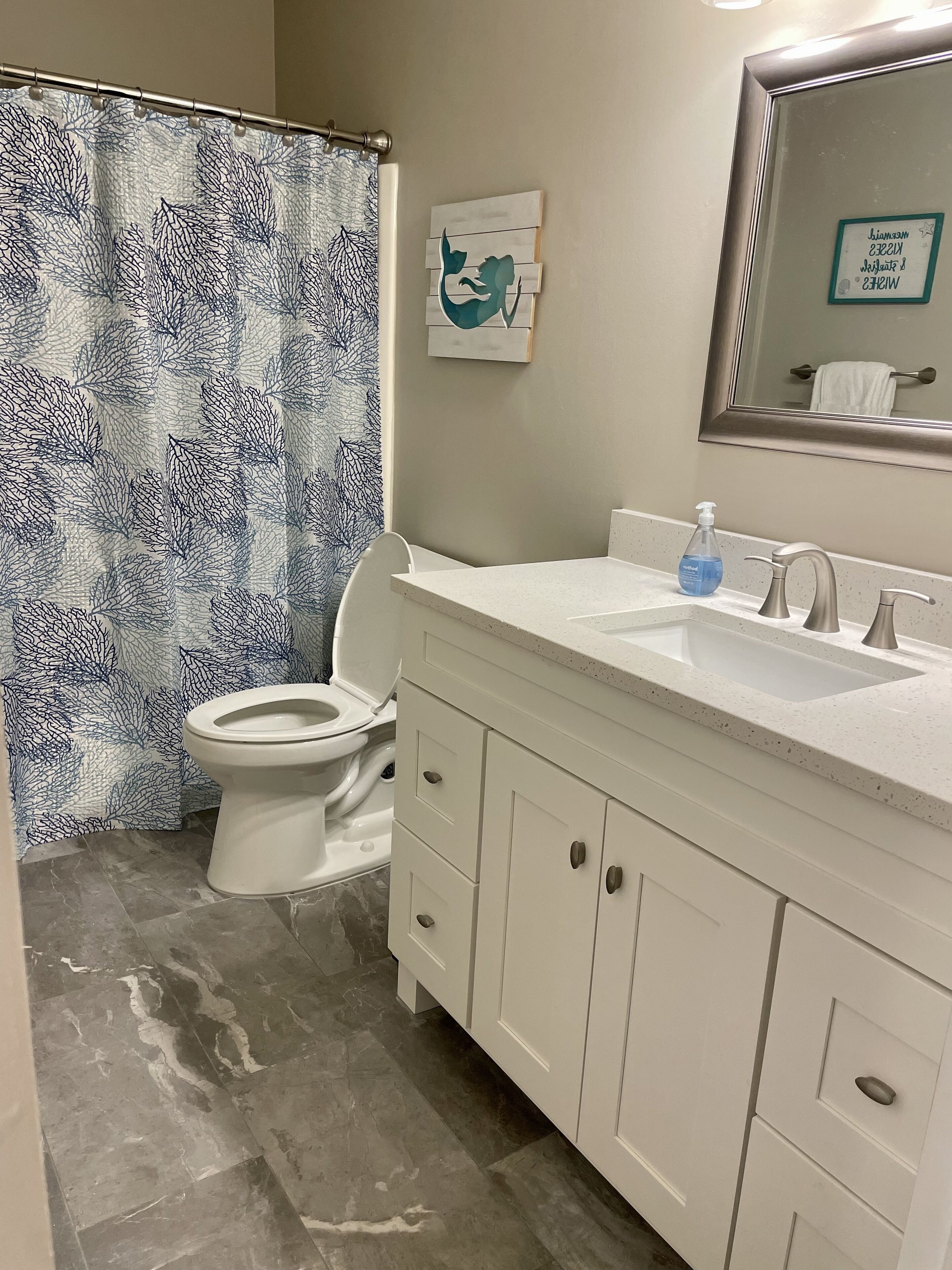 A bathroom with a toilet, a sink with a mirror, and a shower curtain with a leaf pattern.