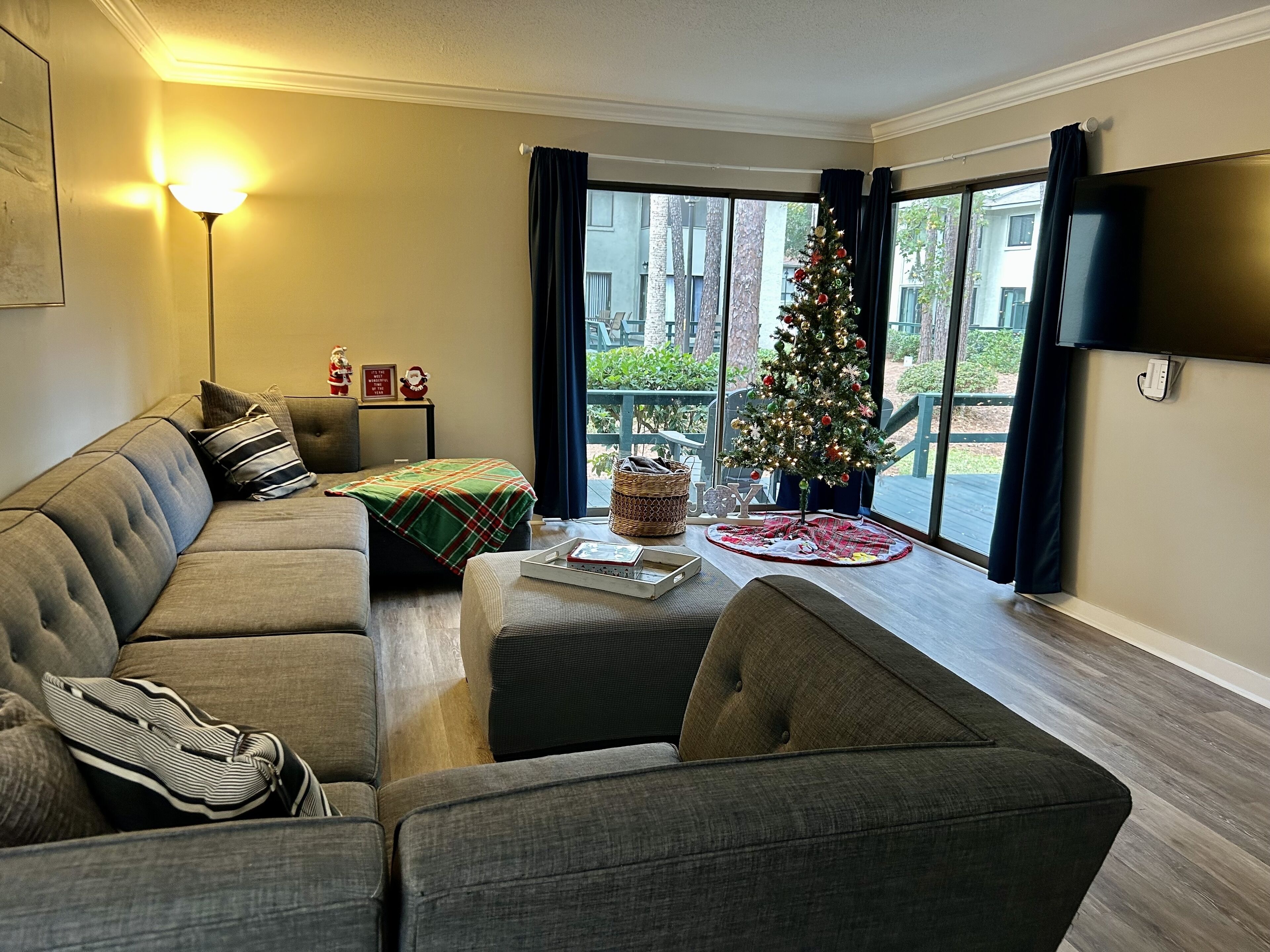 A living room with a grey sofa, a coffee table with a Christmas tree, and a TV mounted on the wall.