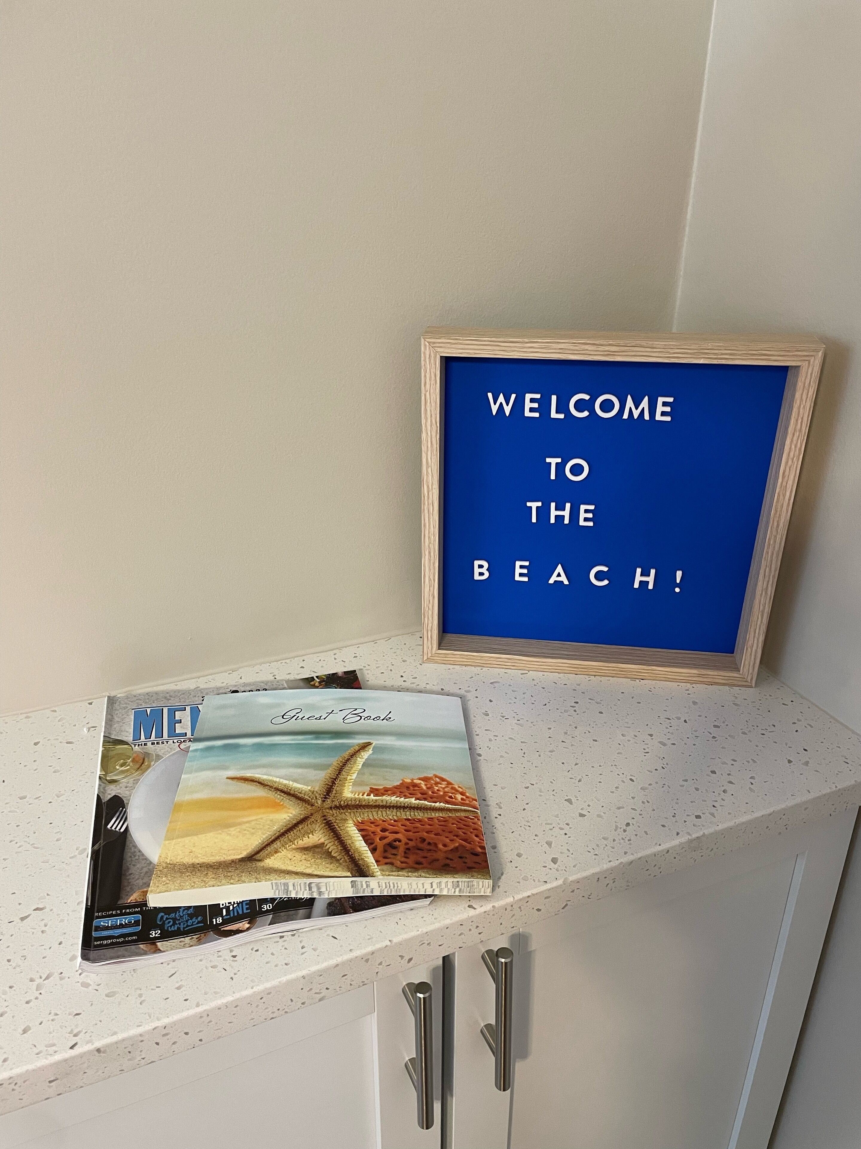 A framed welcome sign and a guest book on a countertop.