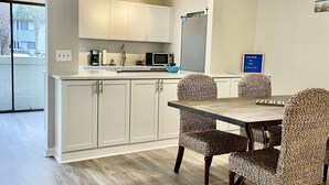 A modern kitchen with white cabinets, a dining area with wicker chairs, and a ceiling fan.