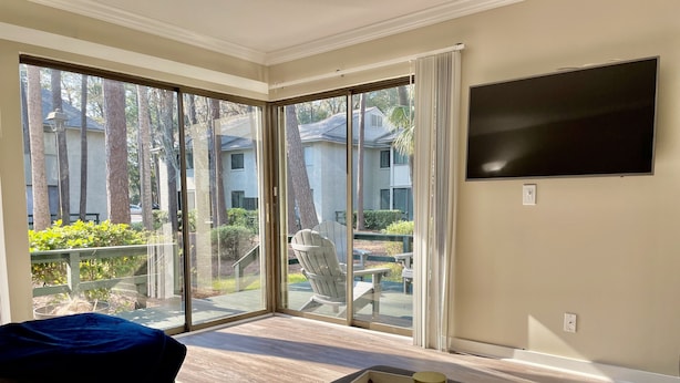 A spacious living room with a large sliding glass door leading to a patio, a flat-screen TV mounted on the wall, and a wooden coffee table with a tray.