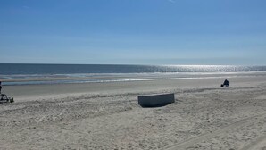 A sandy beach with footprints and tire tracks, a boat, and a person in the distance.