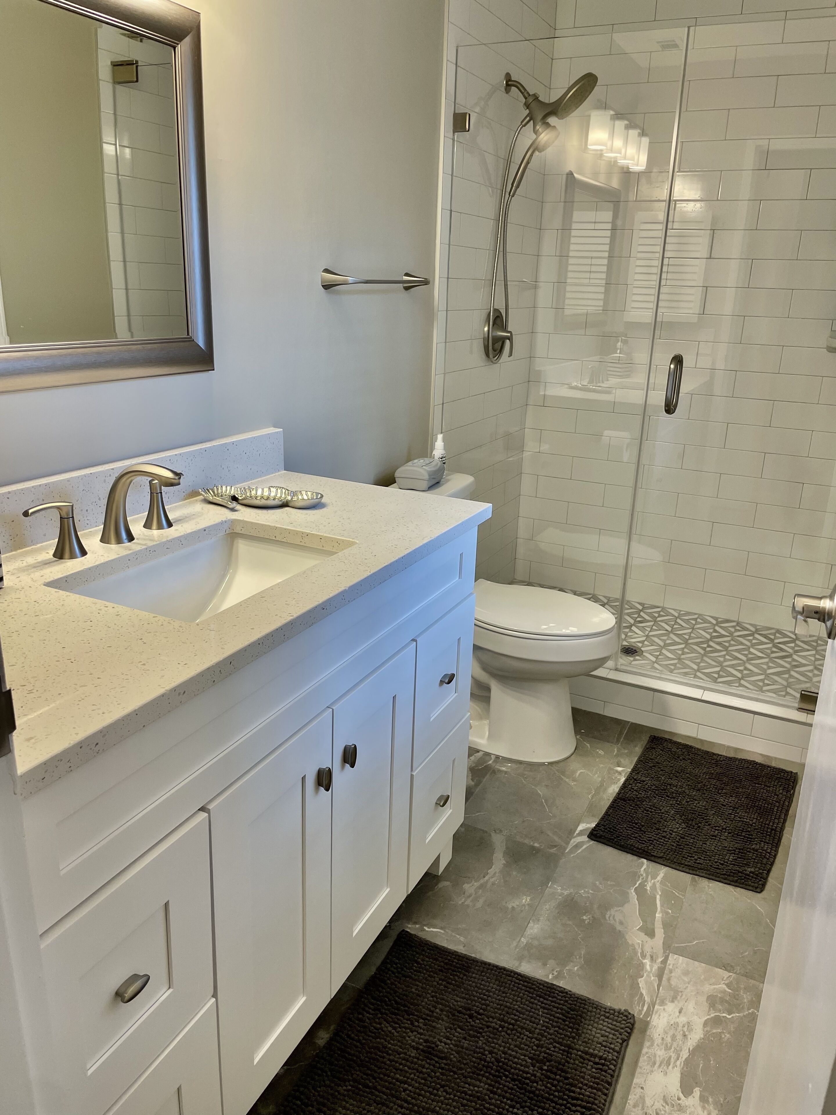 Ein modernes Badezimmer mit einem weißen Waschtisch, einem großen Spiegel, einer Dusche mit Glastür und einer Toilette.