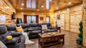 Ein gemütliches Holzhaus-Interieur mit einem ledernen Ecksofa, einem Couchtisch aus Holz und einem an der Wand befestigten Fernseher.