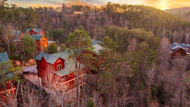 Eine Lodge mit mehreren Gebäuden, umgeben von dichtem Wald, mit einem markanten, roten Gebäude inklusive Balkon.