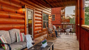 Eine Holzhütte mit einer Holzdiele, einer Couch mit Kissen, einem Schaukelstuhl und einem Tisch mit einem Weinglas.