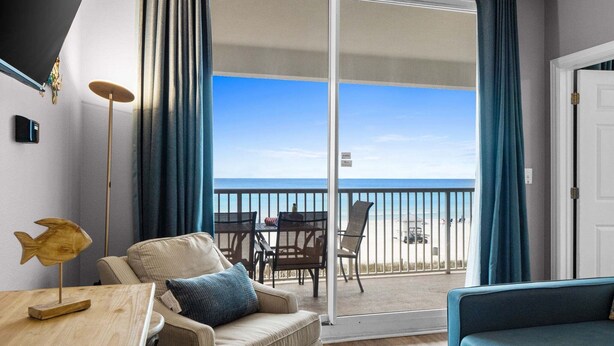 A balcony with a view of the beach, a table with a fish decoration, and a sofa. - Stay Majestic! 3BR w/ Gulf Views, Balcony & Pools (Panama City Beach)