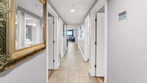 A hotel hallway with white walls, a tiled floor, and a large ornate mirror on the left. - Stay Majestic! 3BR w/ Gulf Views, Balcony & Pools (Panama City Beach)