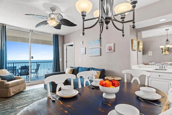 A dining area with a table set for four, a chandelier, and a view of the ocean through large windows.
