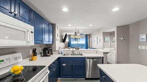 Une cuisine moderne avec des meubles bleus, un plan de travail blanc, des appareils en acier inoxydable et une vue sur l’extérieur.