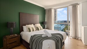 Una habitación de hotel moderna con una cama grande, paredes verdes y un balcón con vista a la ciudad.