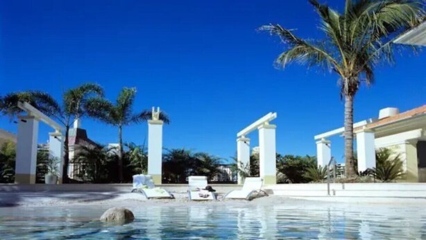 Una piscina azul clara con sillas de descanso y palmeras.