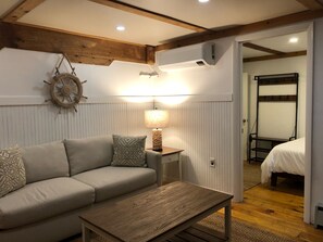 Una habitación acogedora con un sofá, una mesa de centro de madera, una lámpara de pared, un adorno con forma de timón de barco y una cama litera en la habitación contigua.