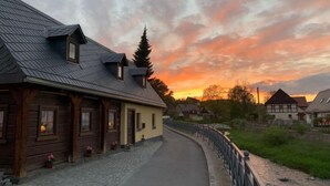 En brostensbelagt sti, der fører til en træbygning med skrå tag og ovenlysvinduer.