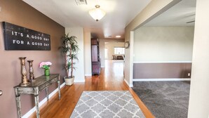 A hallway with a wooden floor, a gray patterned rug, a potted plant, a console table with decorative items, and a sign on the wall. - Desert Pool Retreat (Mesquite)
