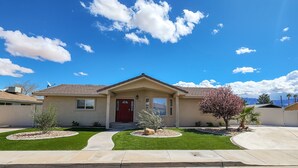 A single-story house with a red door, a front porch, and a well-maintained lawn with landscaping. - Desert Pool Retreat (Mesquite)