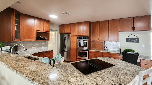 A modern kitchen with granite countertops, stainless steel appliances, and wooden cabinetry. - Desert Pool Retreat (Mesquite)