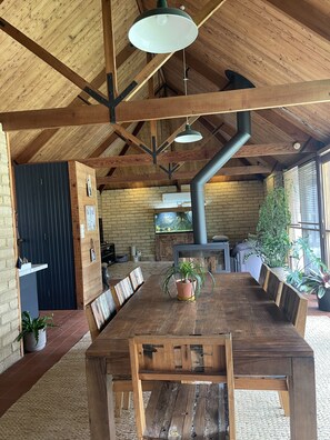 A rustic wooden dining area with a large table and benches, a hanging light fixture, and a brick wall with a fireplace.