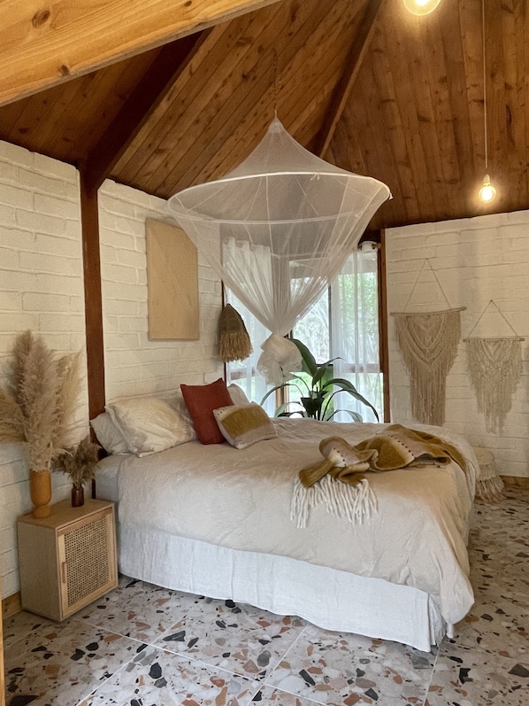 A bedroom with a bed, a canopy, a plant, and a wall-mounted macrame piece.