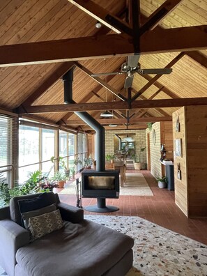A cozy living room with a fireplace, wooden beams, and large windows.