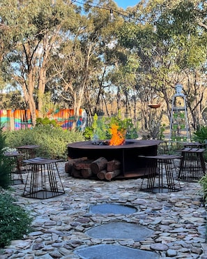 An outdoor seating area with a fire pit surrounded by stone tiles, metal tables, and chairs.