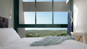 Ein Schlafzimmer mit großem Fenster, einem Bett mit weißen Leinen, einer grauen Strickdecke und einer Pendelleuchte.
