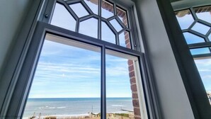 Vista attraverso una finestra con un motivo geometrico, su una spiaggia e l'oceano.