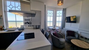 Una cucina moderna con un'isola grande, zona pranzo con un tavolo rotondo e vista sul mare attraverso ampie finestre.