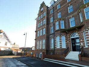 A multi-story brick building with a central entrance, large windows, and a staircase leading to the entrance. - With its wonderful, far reaching sea views, this first floor apartment certainly does have the WOW f (Sheringham)