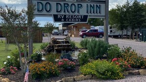 A sign for 'Do Drop Inn RV Resort & Cabins' with a decorative emblem and a waterfall feature in the foreground. - Do Drop Inn RV Resort and Cabins (Cartwright)
