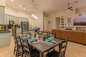 Una cucina moderna con elettrodomestici integrati, una zona pranzo con tavolo apparecchiato e un soggiorno con TV e scaffalature.