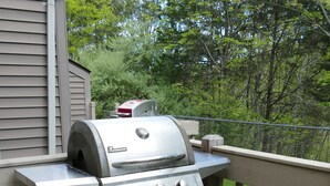 Ein Grill mit Beistelltisch und gepolstertem Stuhl auf einer Holzterrasse.