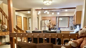 Ein Wohnzimmer mit Ecksofa, Glastisch und einer Küche im Hintergrund.