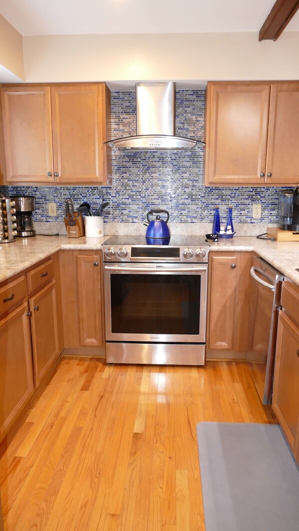 A modern kitchen with wooden cabinets, a stainless steel range, and a blue kettle on the countertop.