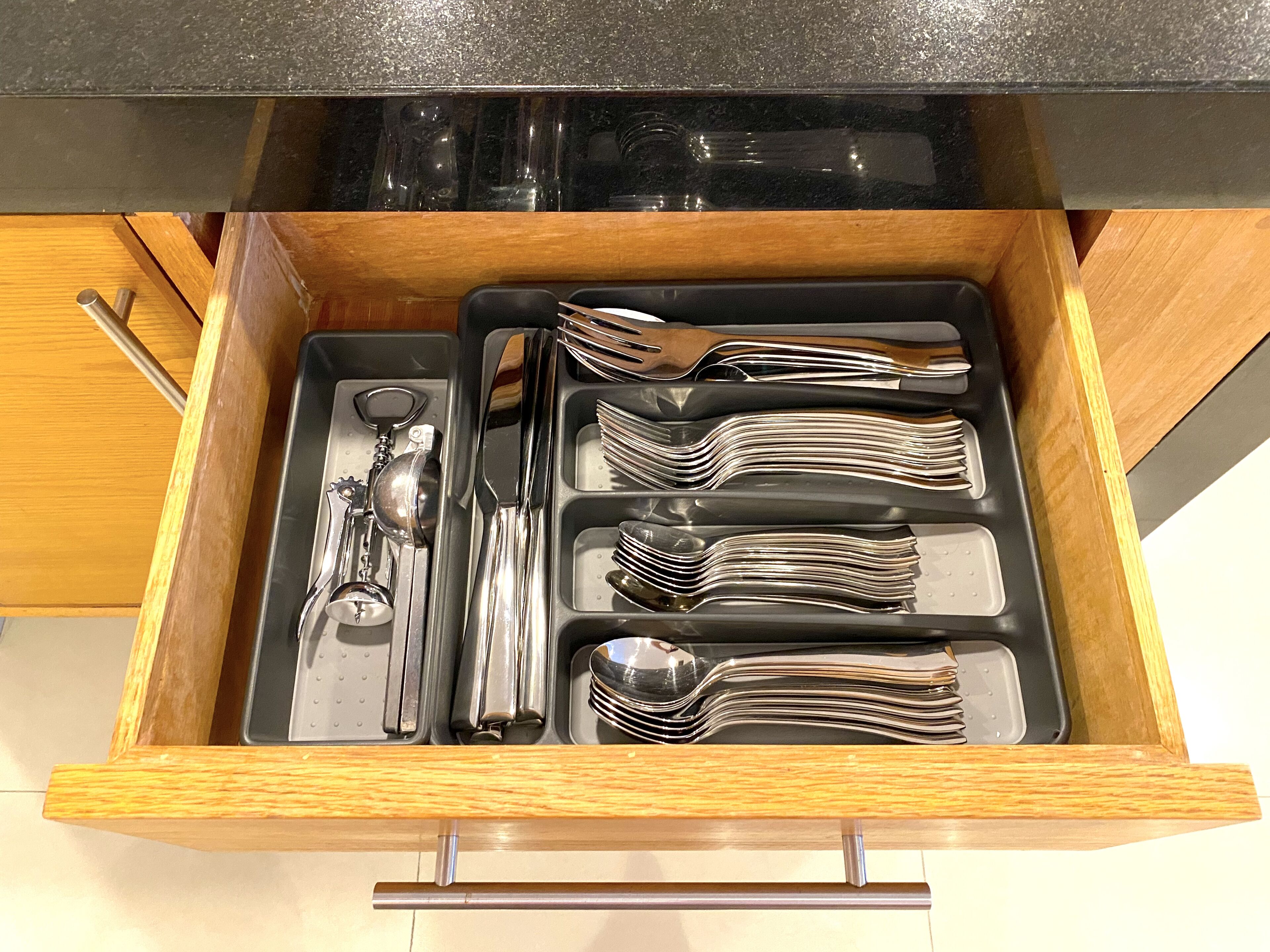 A drawer with neatly organized silverware, including forks, spoons, and a bottle opener.