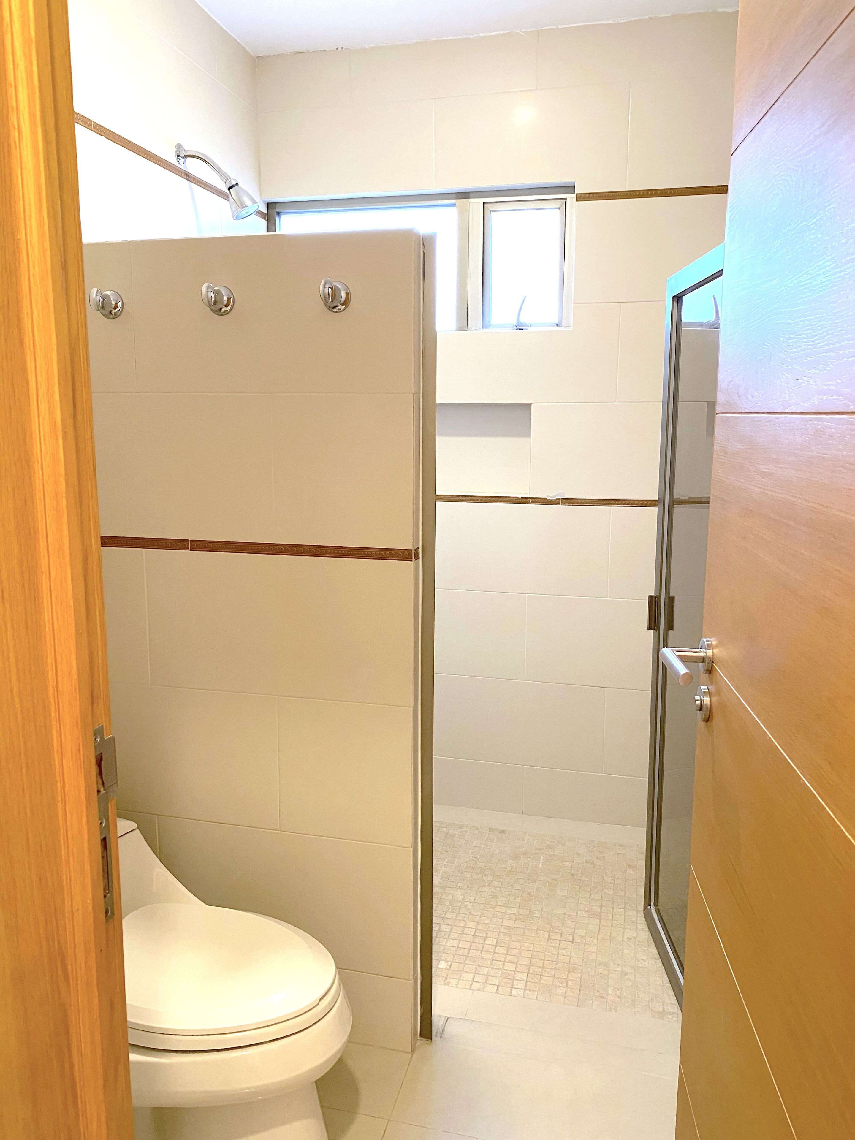 A bathroom with a shower, toilet, and a window above the shower.
