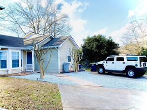 A house with a driveway, a white SUV parked in front, and a tree in the yard.