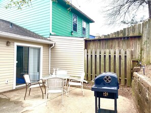 A backyard with a patio table and chairs, a barbecue grill, and a wooden fence.