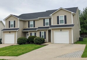 A two-story residential building with a front garage, a covered driveway, and a well-maintained lawn.