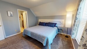 A bedroom with a bed, a nightstand, a lamp, and a door leading to another room.