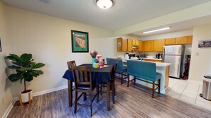 A dining area with a table set for four, wooden chairs, a potted plant, and a framed picture on the wall.