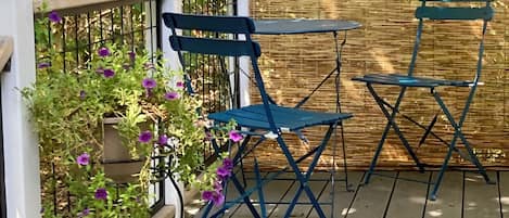 A wooden deck with blue folding chairs and a small table, surrounded by a white fence and dense foliage.