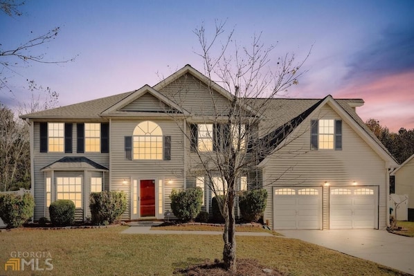 A two-story house with a red front door, multiple windows, and a garage.