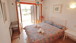 A bedroom with a bed, a bedside table, a small table, and a window with curtains. - Jane - modern, well-equipped bungalow in Moraira (Teulada)