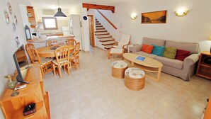 A spacious living area with a sofa, coffee table, and dining table. A staircase leads to an upper floor. - Jane - modern, well-equipped bungalow in Moraira (Teulada)